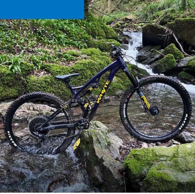 Dark blue Whyte full-suspension mountain bike beside rocky stream