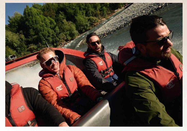 Three men in life jackets riding a jet boat on a river