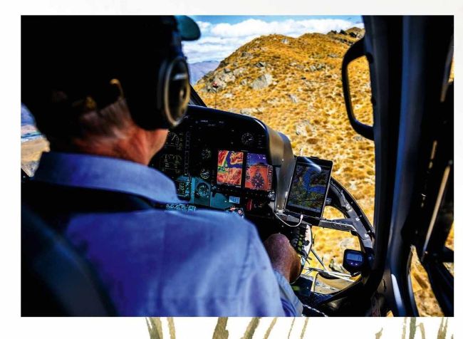 Helicopter pilot at controls flying over mountainous New Zealand terrain