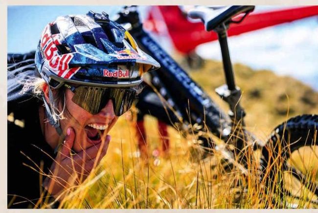 Close-up of smiling Red Bull helmeted mountain biker lying in tussock grass