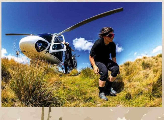 Mountain biker crouching on hillside with helicopter landed behind them