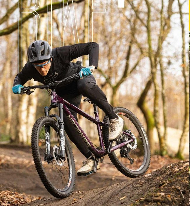 Mountain biker cornering hard on a woodland trail on purple hardtail