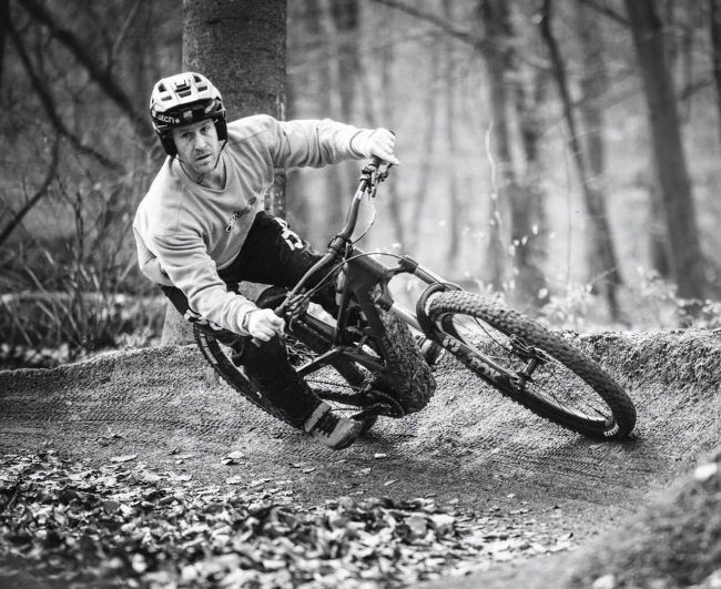 Rider carving berm on mountain bike in forest, black and white