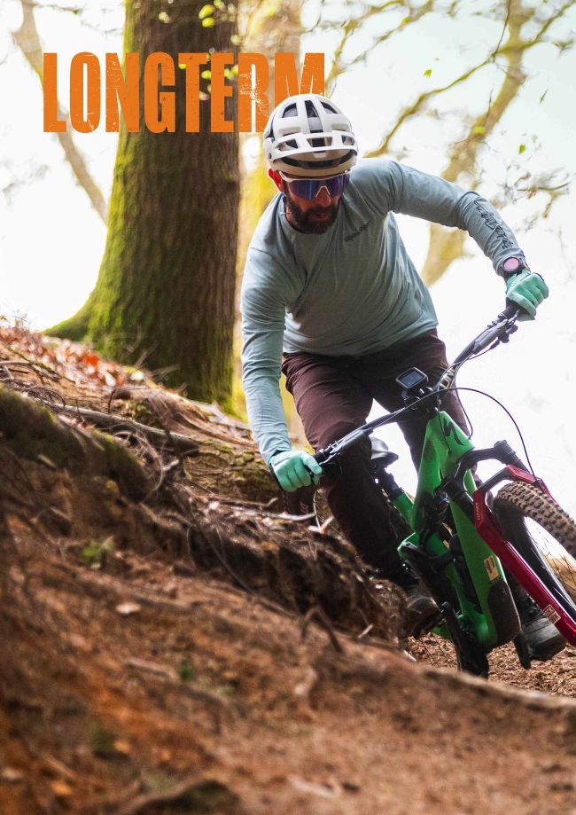 Mountain biker riding green e-bike down rooty forest trail