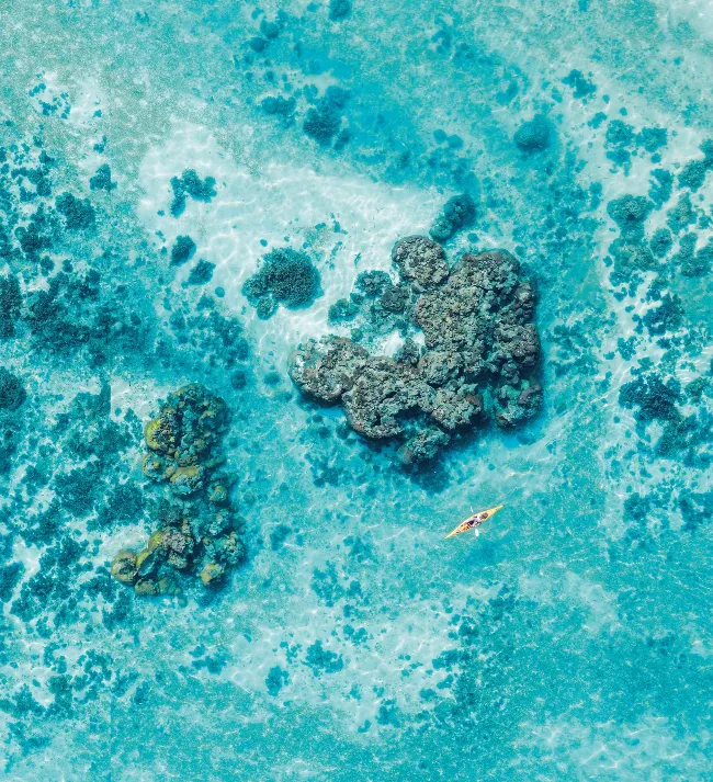 Aerial view of a yellow sea kayak paddling through vivid turquoise shallow water above dark coral reef formations at Ningaloo.